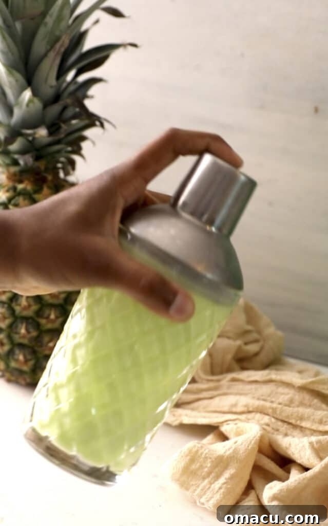 A hand vigorously shaking a cocktail shaker, mixing the Scooby Snack Shot ingredients to chill and combine them.