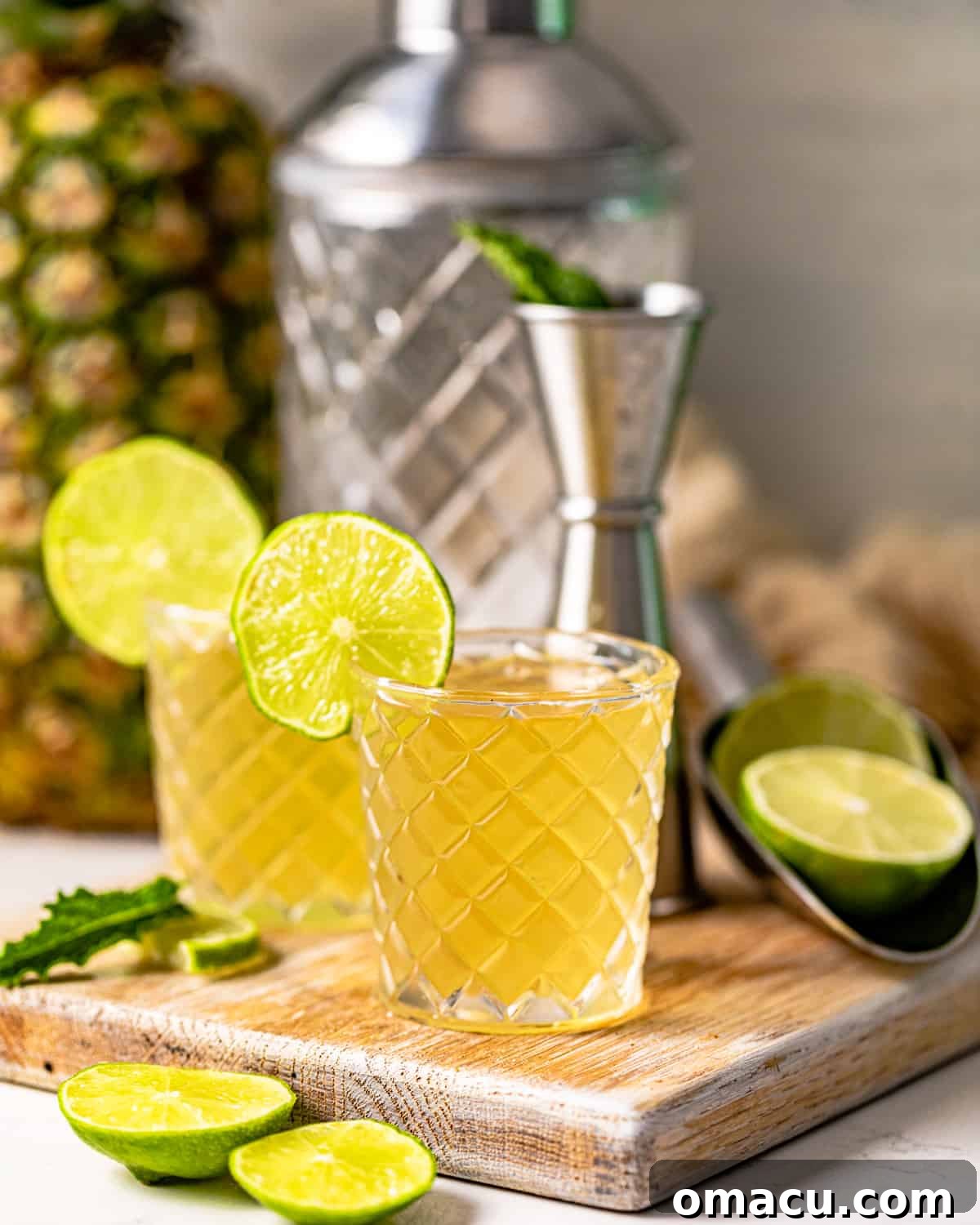 Two Water Moccasin shots served in elegant shot glasses on a wooden board, with a cocktail shaker in the background, ready for a party.