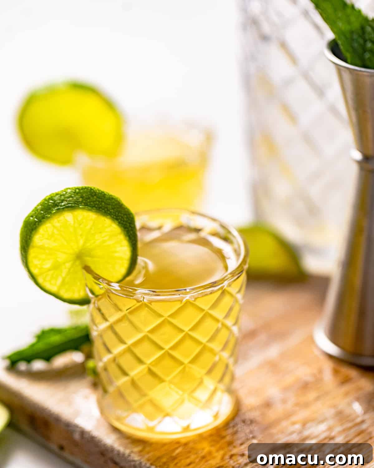 A single Water Moccasin shot in a clear shot glass, garnished with a fresh lime wedge, resting on a rustic wooden surface.