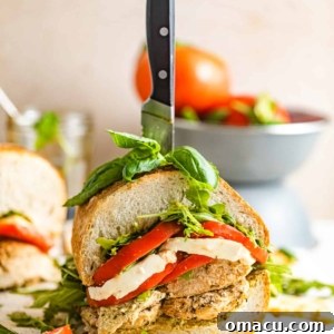 A sliced chicken caprese sandwich in front of a bowl of tomatoes.