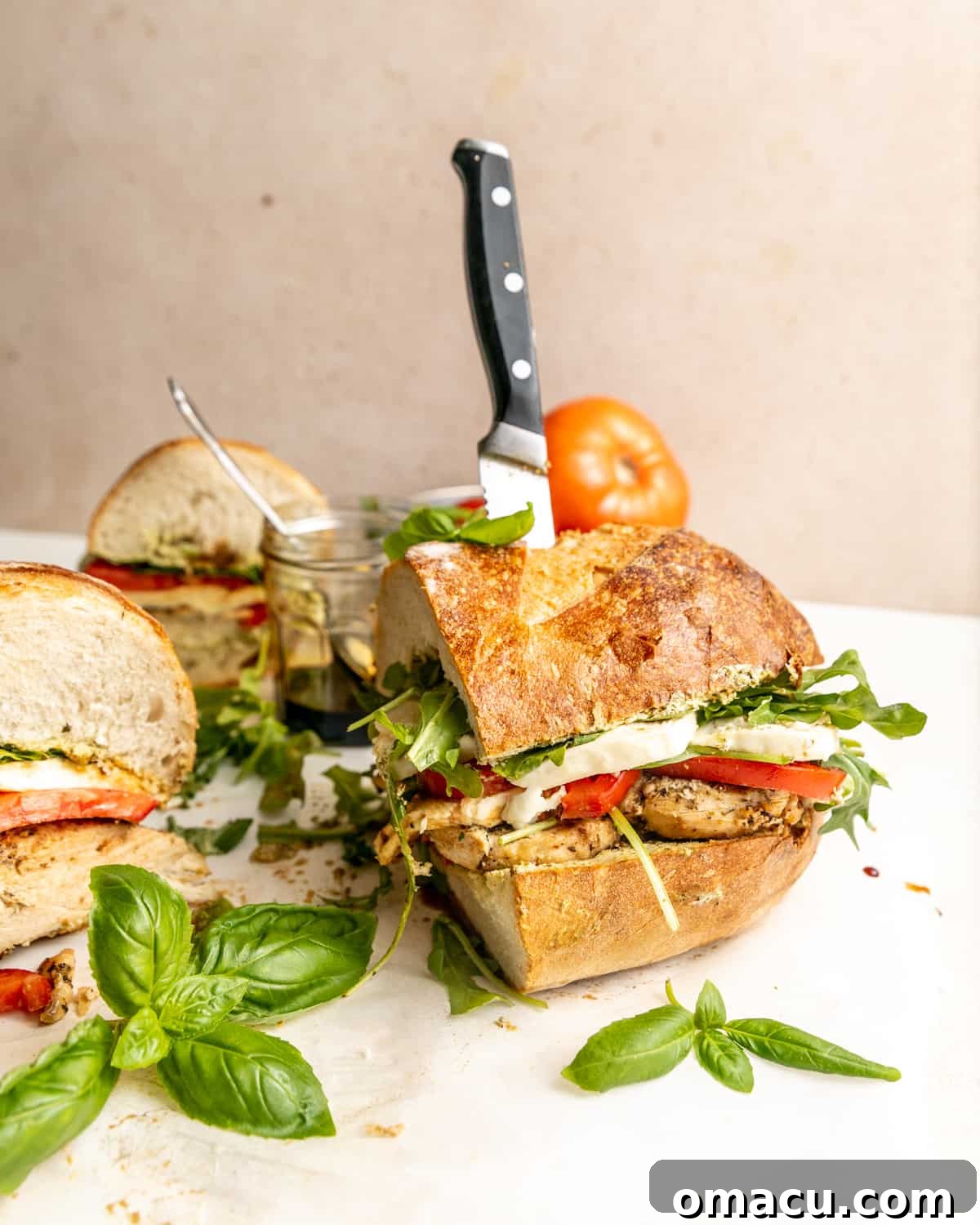 A side profile photograph of a delectable Chicken Caprese Sandwich, artfully propped up by a knife, standing tall to showcase its beautifully layered ingredients.