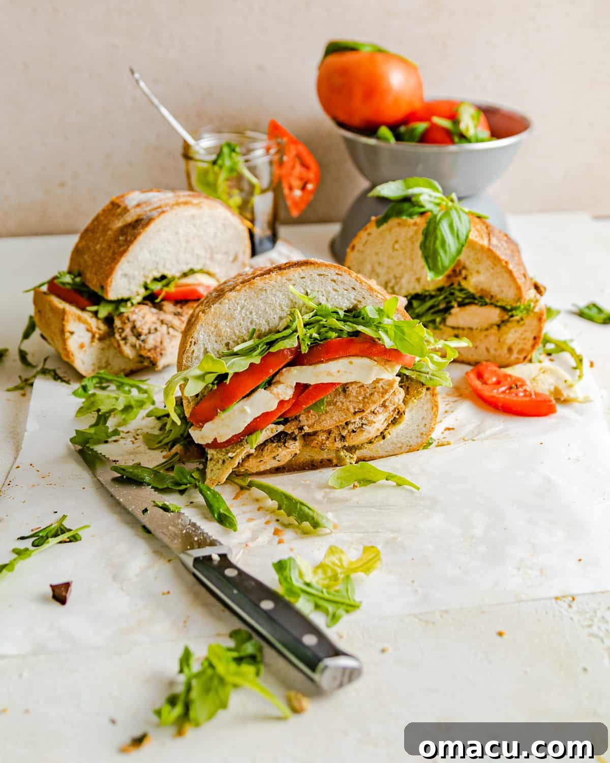 A meticulously cut chicken caprese sandwich, presented next to a rustic bowl of vibrant tomatoes and a small serving of glistening homemade balsamic glaze, ready for drizzling.