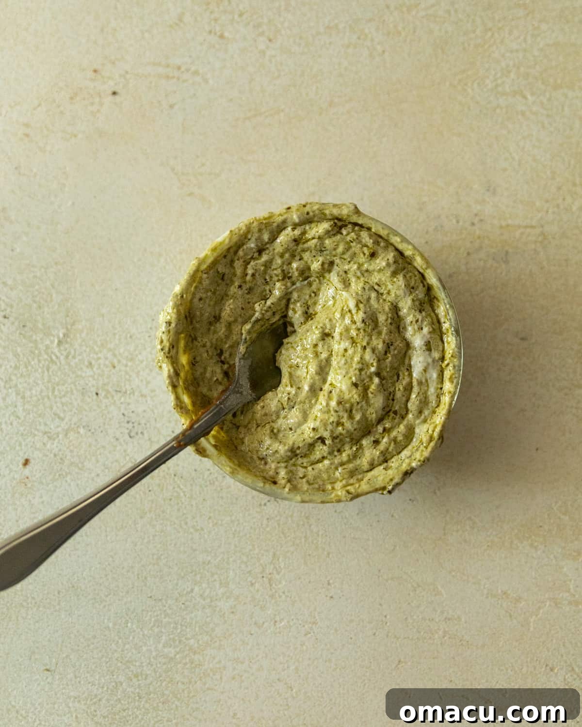 A small bowl containing a creamy mixture of vibrant pesto and rich mayonnaise, perfectly blended into a delicious spread.