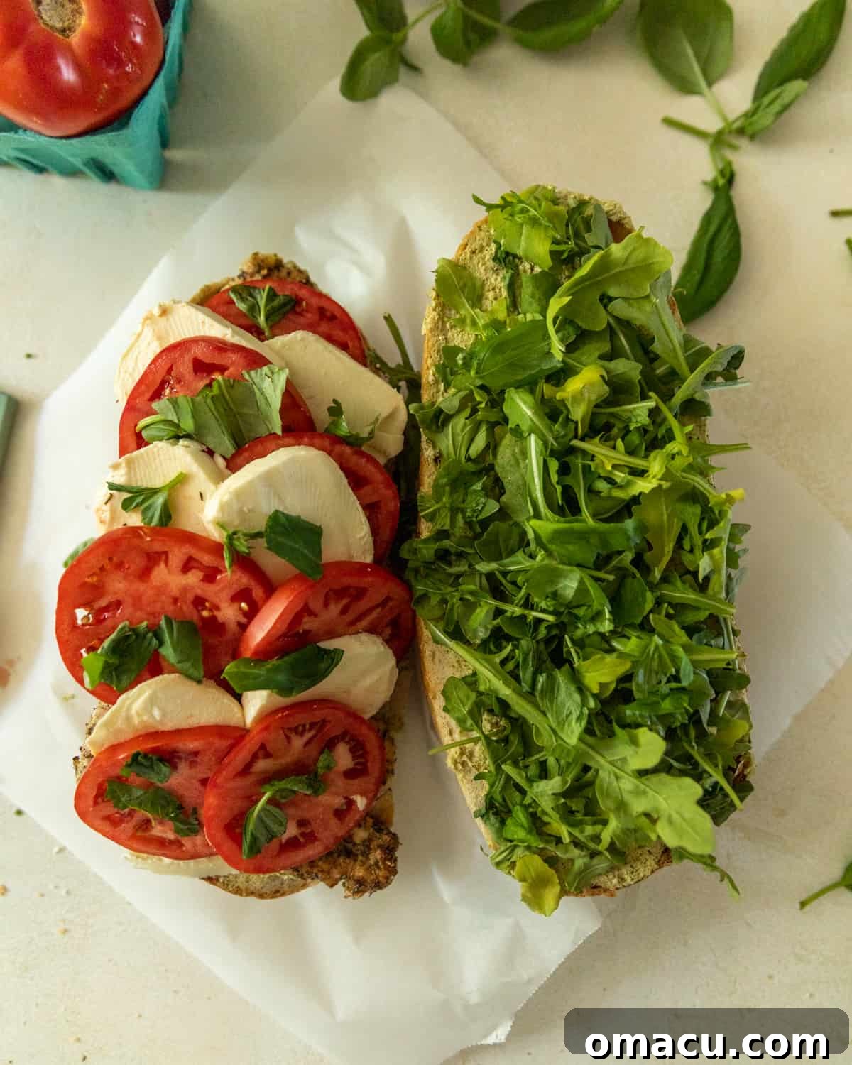 A half-cut sandwich showcasing fresh arugula on one side and a delightful arrangement of vibrant tomatoes, creamy fresh mozzarella, and fragrant basil on the other, revealing its rich interior.