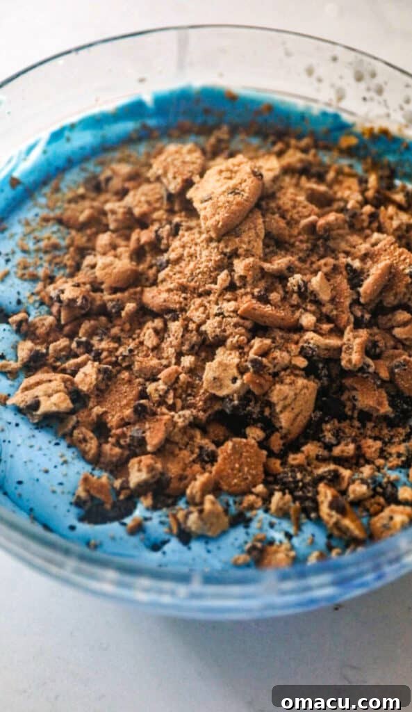 crushed chocolate chip cookies being folded into the blue whipped cream.