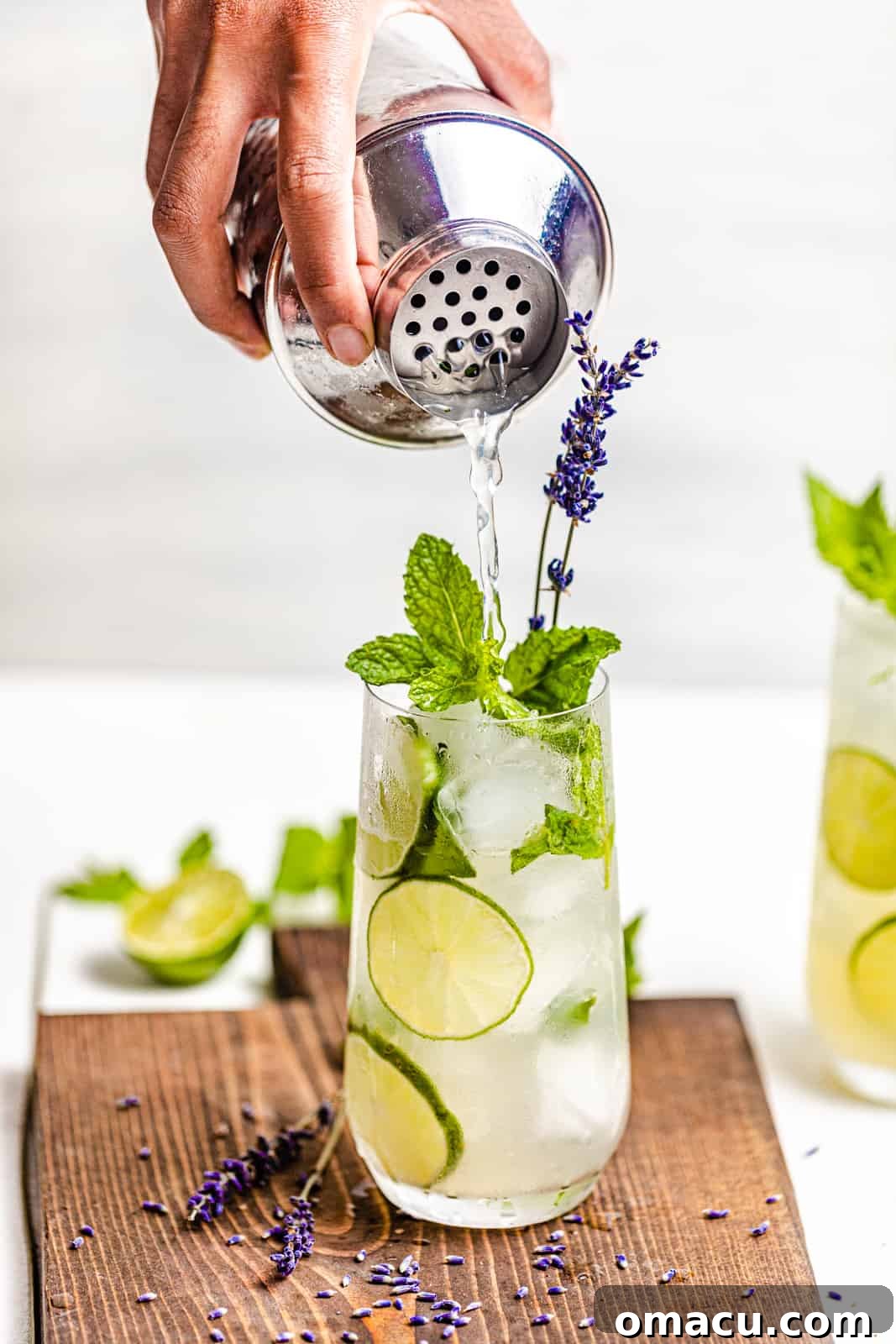 A close-up shot of a hand expertly pouring a freshly shaken gin mojito from a sleek cocktail shaker into a chilled highball glass filled with ice.
