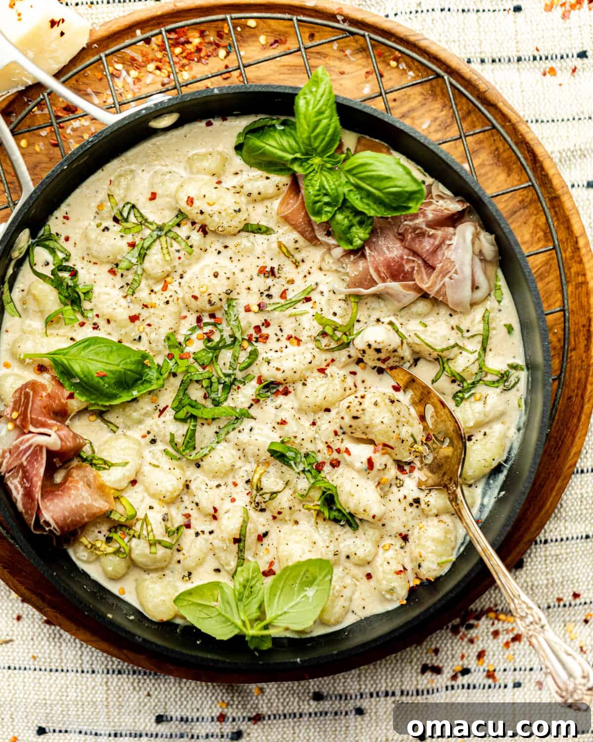 Creamy cacio e pepe gnocchi served in a pan, garnished with fresh basil leaves and crispy prosciutto.
