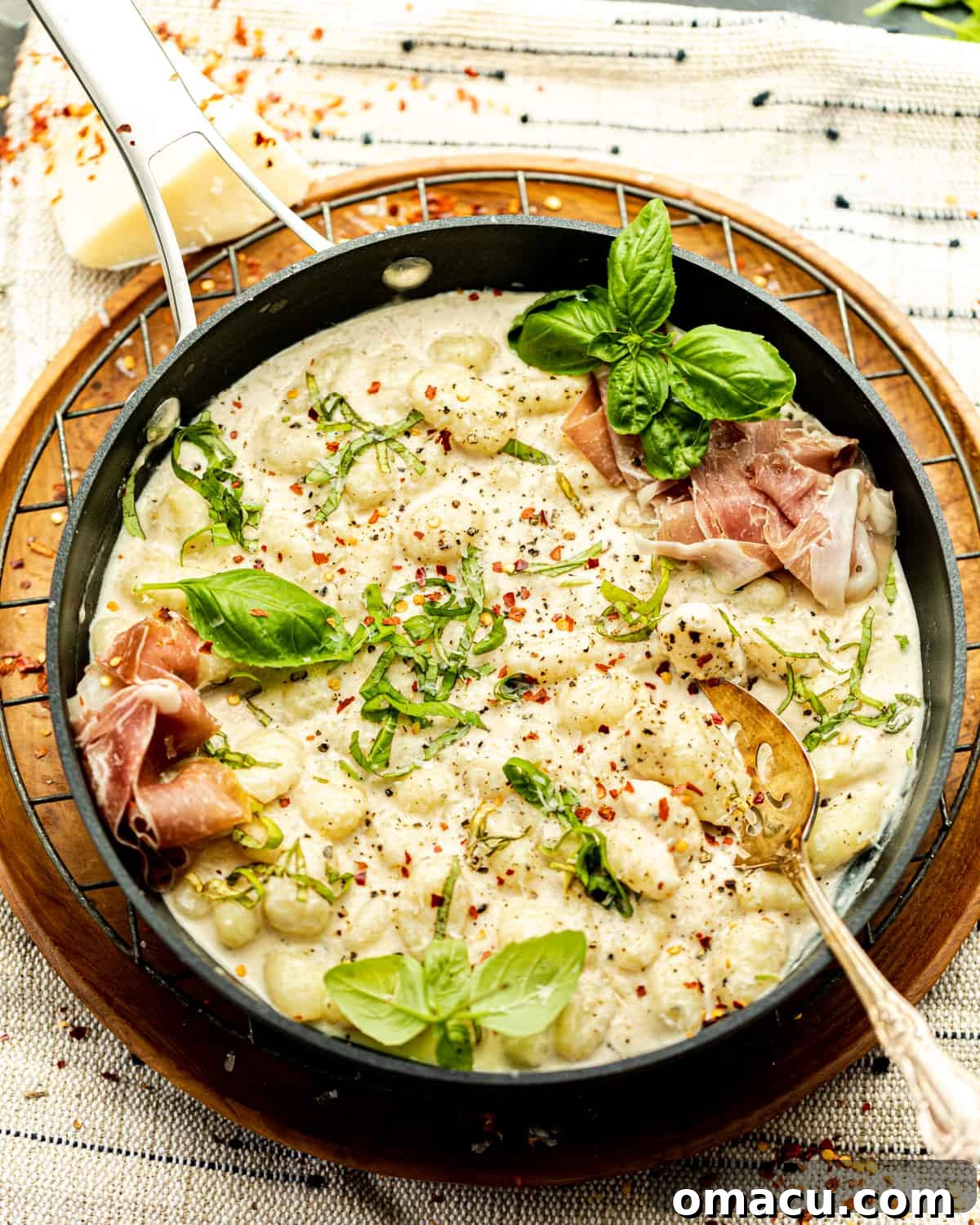 Finished cacio e pepe gnocchi in a skillet, adorned with prosciutto and fresh basil.