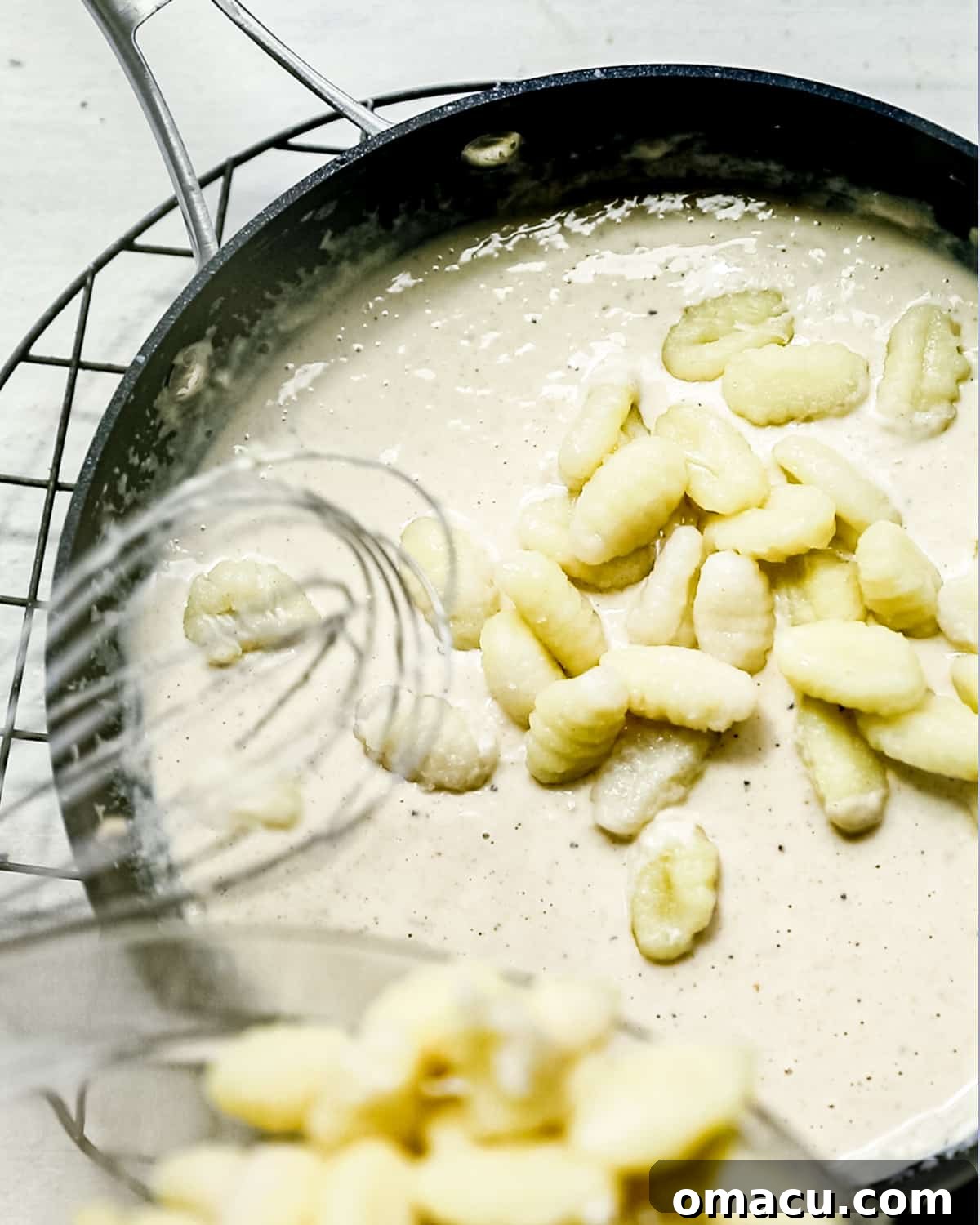 Gnocchi being gently folded into the creamy cacio e pepe sauce in a skillet.