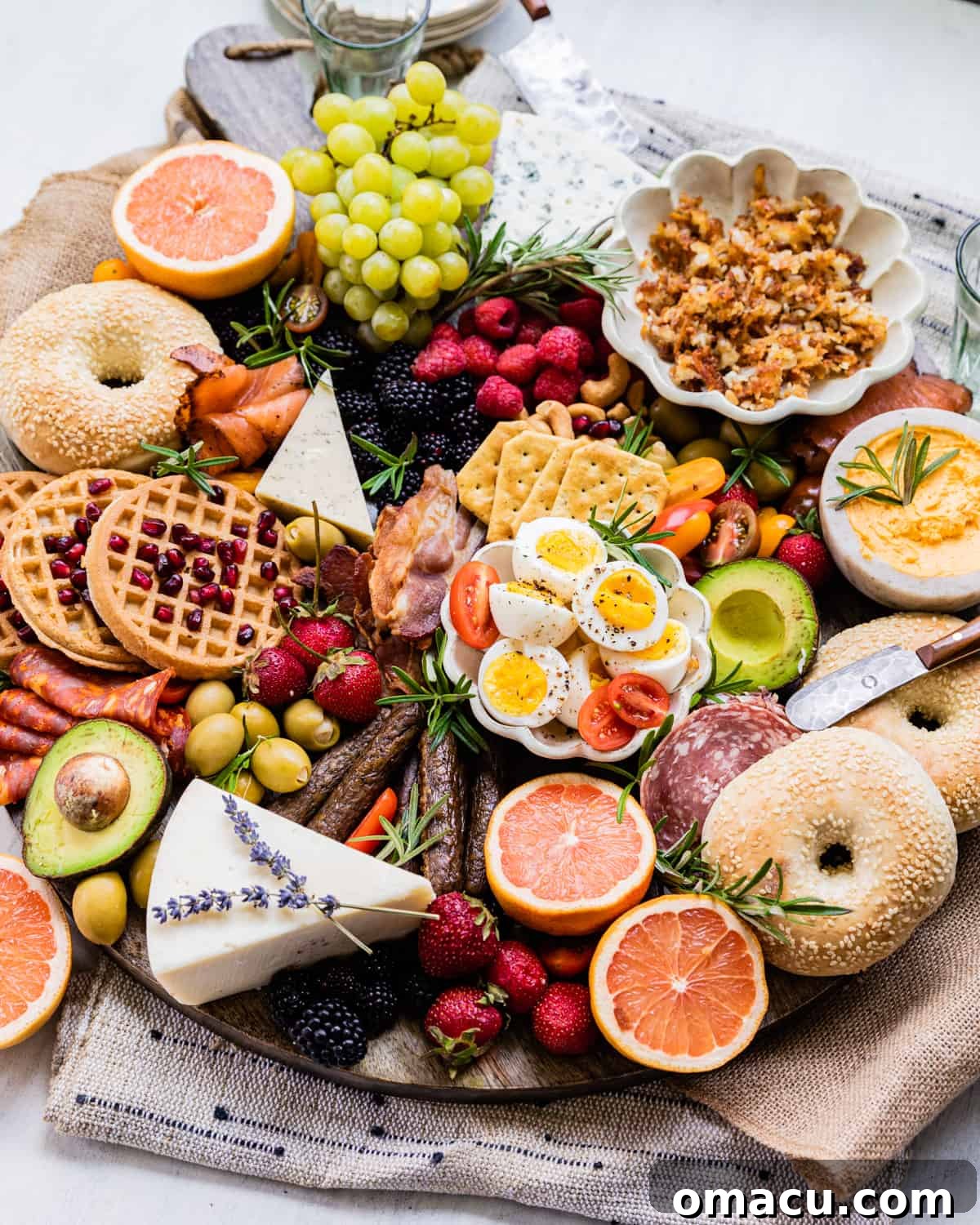 A breakfast charcuterie board filled with bagels, waffles, fresh fruit, cheeses, and cured meats, beautifully arranged.