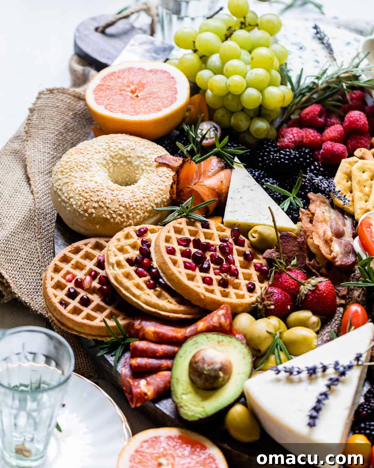 An up-close photo of a breakfast charcuterie board showcasing fluffy waffles topped with vibrant pomegranate arils and juicy sliced grapefruit.
