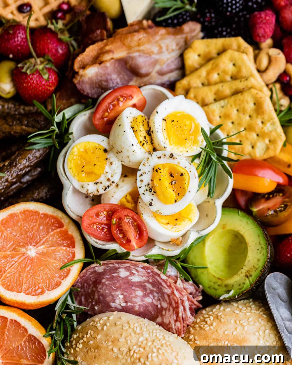 An up-close photo of jammy eggs nestled in a small bowl, surrounded by crackers, sliced avocado, and vibrant fresh fruit on a charcuterie board.