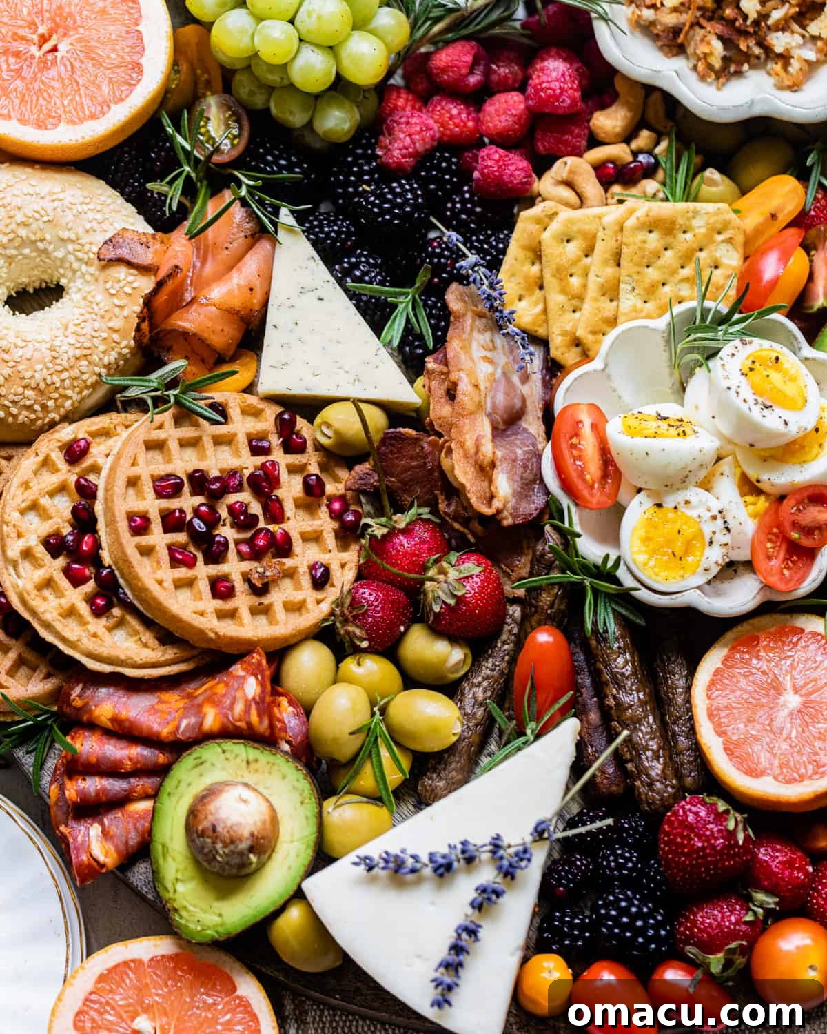 The vibrant ingredients of a breakfast charcuterie board laid out – cured meats, fresh fruit, various cheeses, hard-boiled eggs, olives, and golden waffles, ready for assembly.