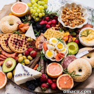 A breakfast charcuterie board filled with bagels, waffles, fresh fruit, cheeses, and cured meats.
