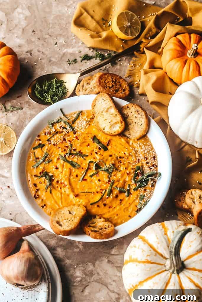 A vibrant bowl of roasted red pepper and pumpkin soup, garnished with fresh sage, surrounded by decorative pumpkins and autumn-themed plates, evoking a sense of fall comfort.