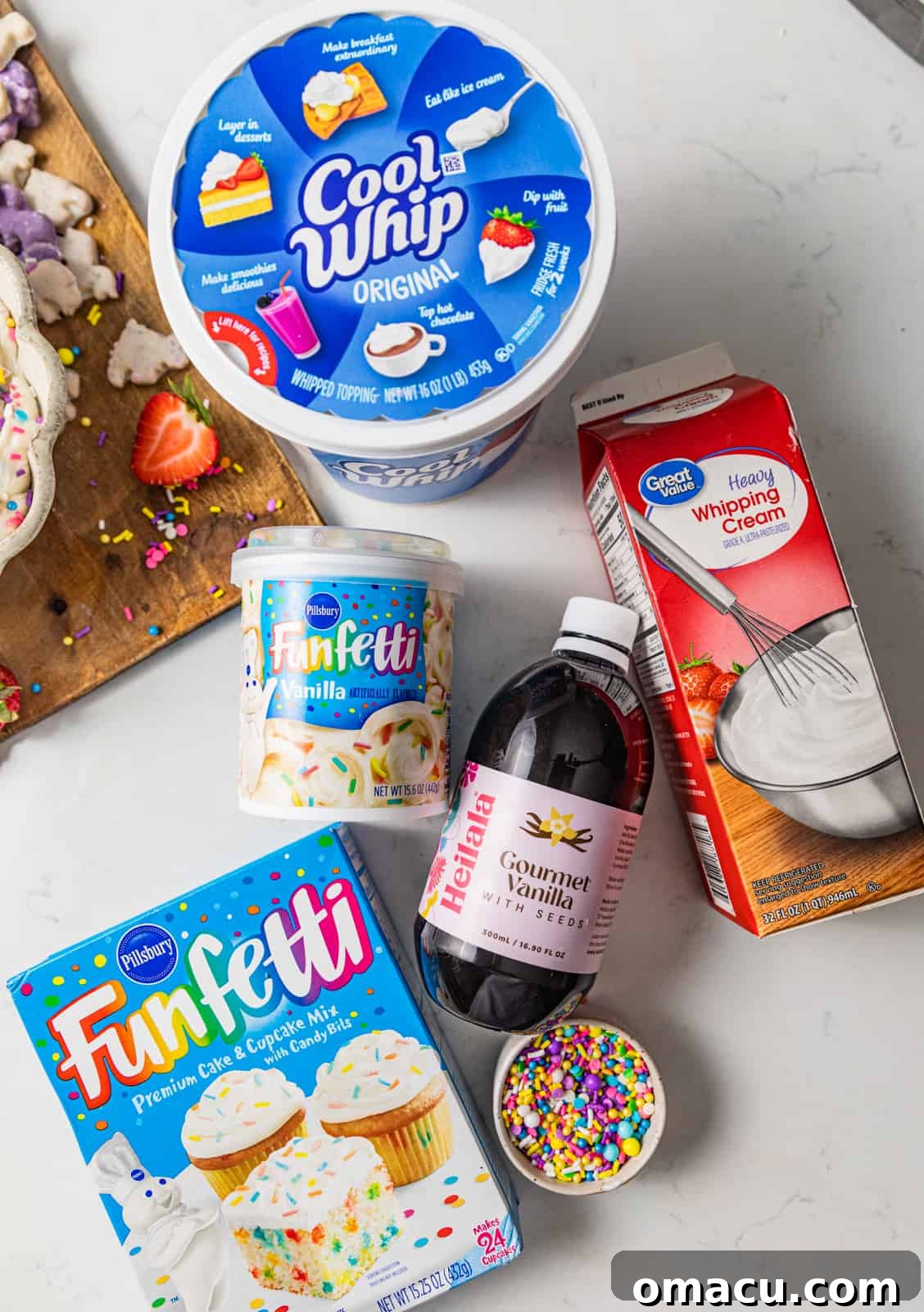 A flat lay photograph showcasing all the essential ingredients for making homemade Dunkaroo Dip: Cool Whip, heavy cream, vanilla extract, a box of funfetti cake mix, a tub of funfetti vanilla frosting, and a generous amount of rainbow sprinkles.
