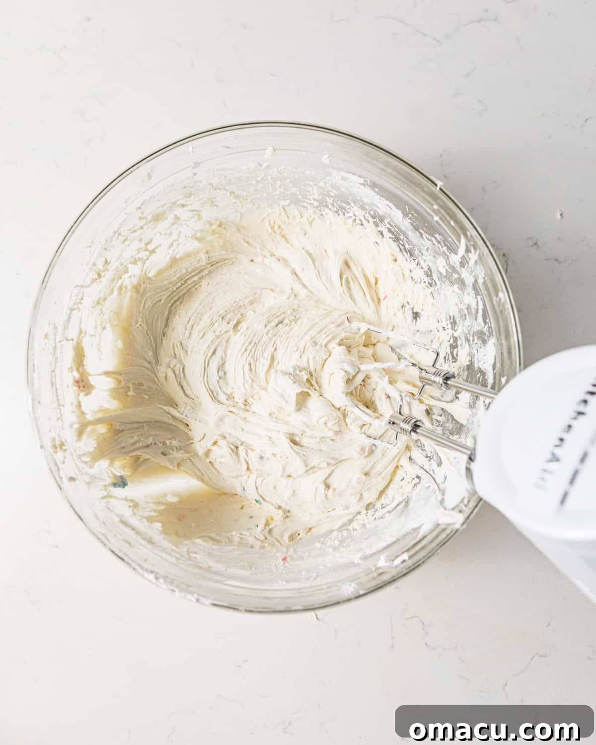 Cool Whip and funfetti cake mix being vigorously mixed together in a large bowl with an electric mixer, creating a smooth base for the dip.