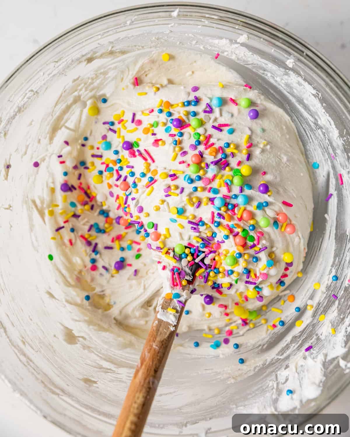 A spatula gently folding vibrant rainbow sprinkles into the creamy, homemade Dunkaroo Dip mixture, ensuring even distribution without color bleed.