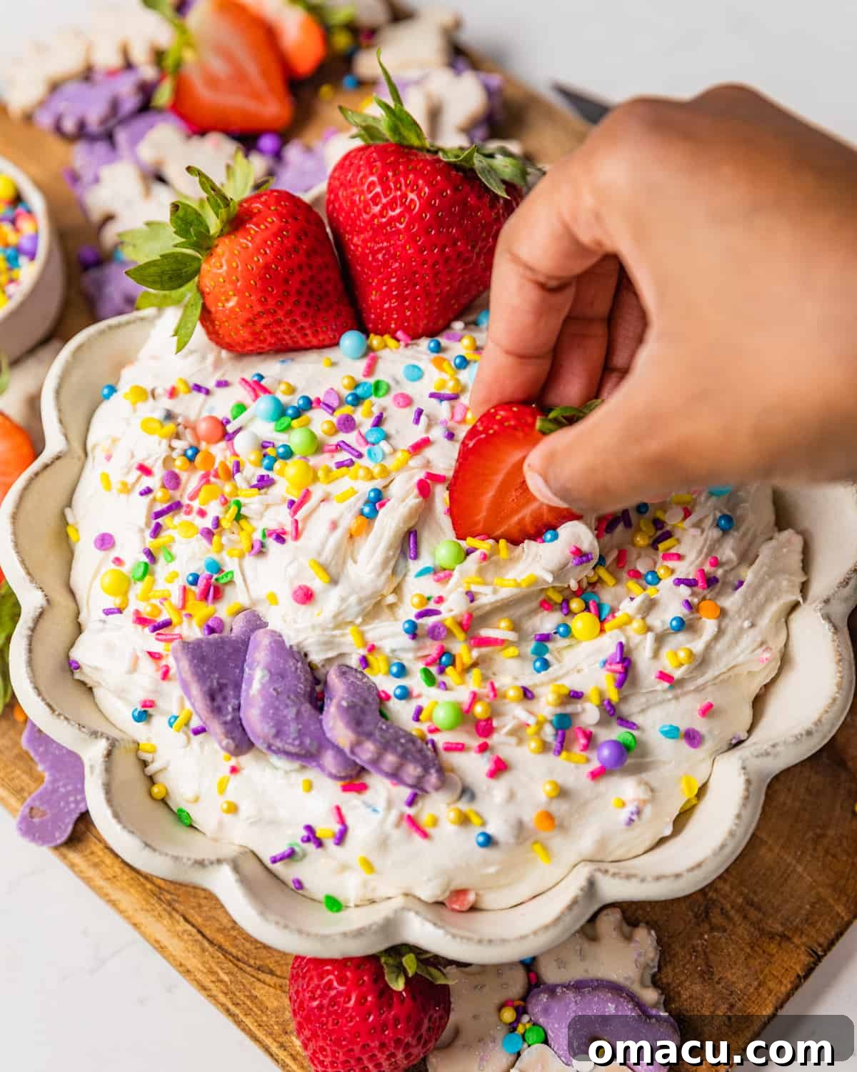 A hand dipping a fresh, juicy strawberry into a bowl of creamy homemade Dunkaroo Dip, highlighting the dip's perfect consistency and inviting texture.