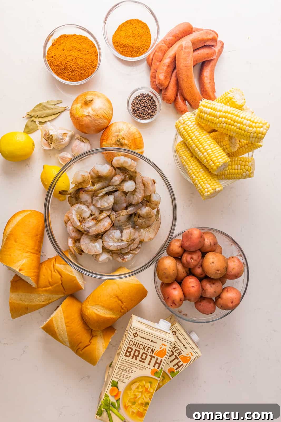 ingredients to make low country boil - shrimp, water, chicken broth, onions, lemons, garlic, old bay seasoning, cajun seasoning, peppercorns, bay leaves, corn, smoked sausage, red potatoes, and bread.