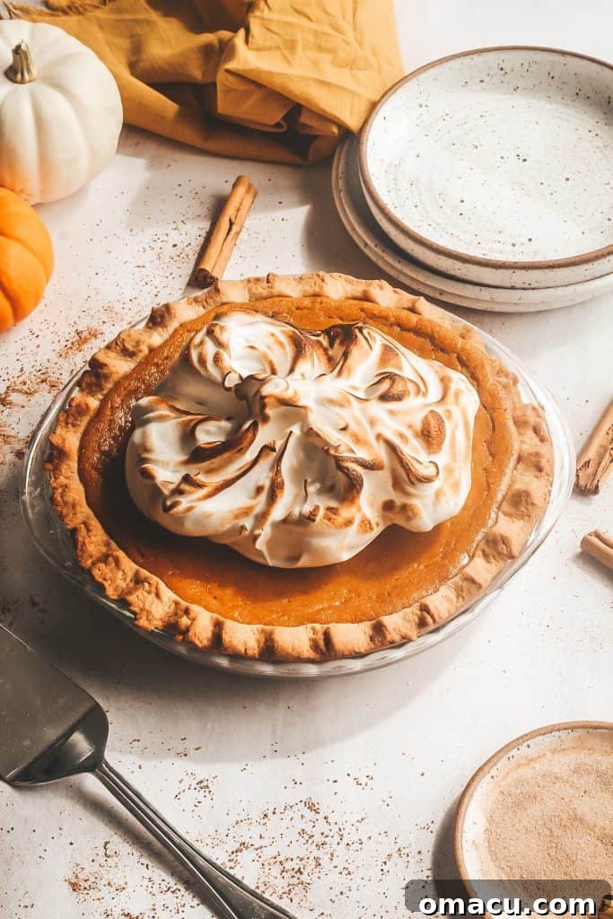 Sage Browned Butter Pumpkin Pie set on a rustic table with decorative pumpkins and plates in the background, highlighting its autumnal charm.