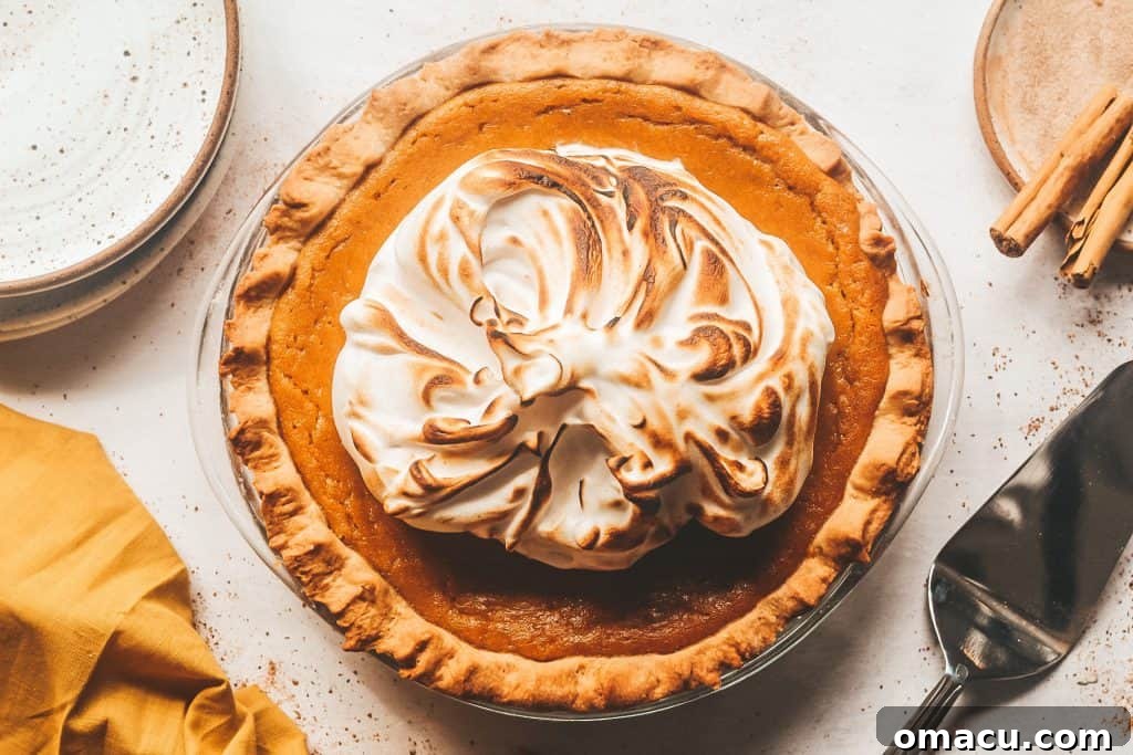 A delicious slice of pumpkin pie topped with spiced meringue, served on a plate with elegant utensils, ready to be enjoyed.