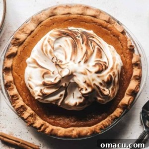 A close-up of a beautifully finished pumpkin pie with a generous topping of spiced meringue, ready to be served.