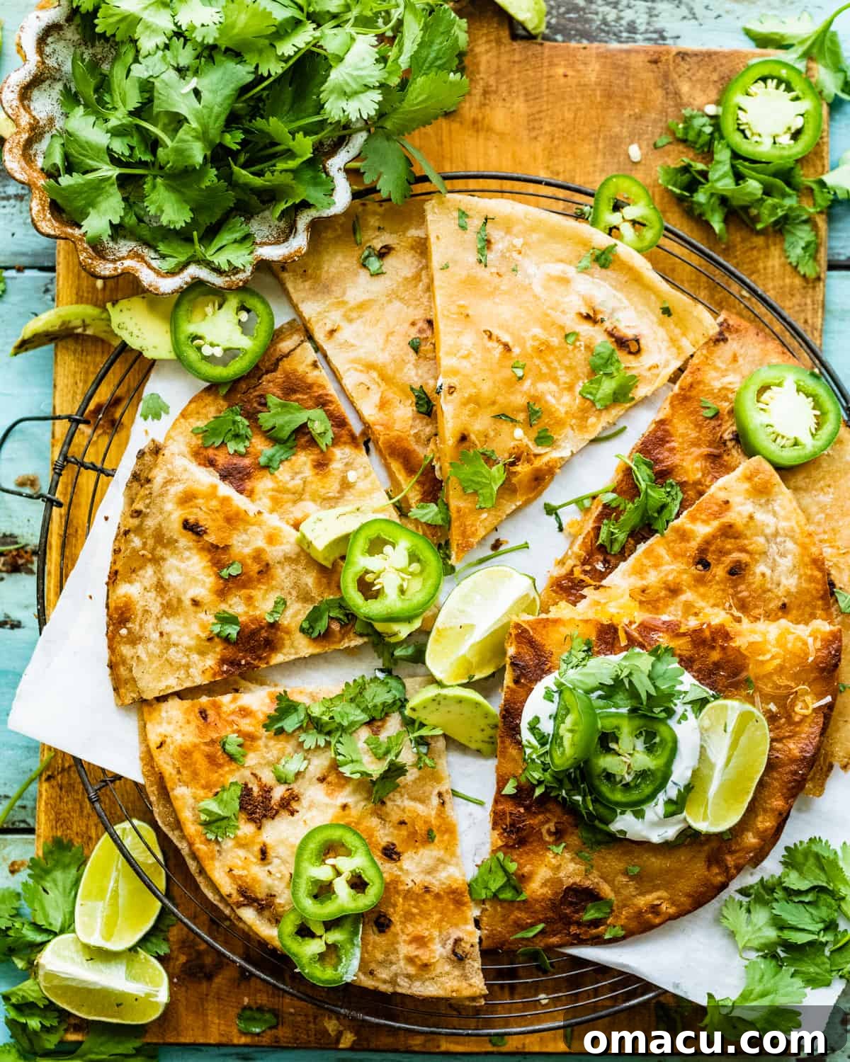 cheese quesadilla on a cooling rack garnished with sliced jalapeños, cilantro, and limes.