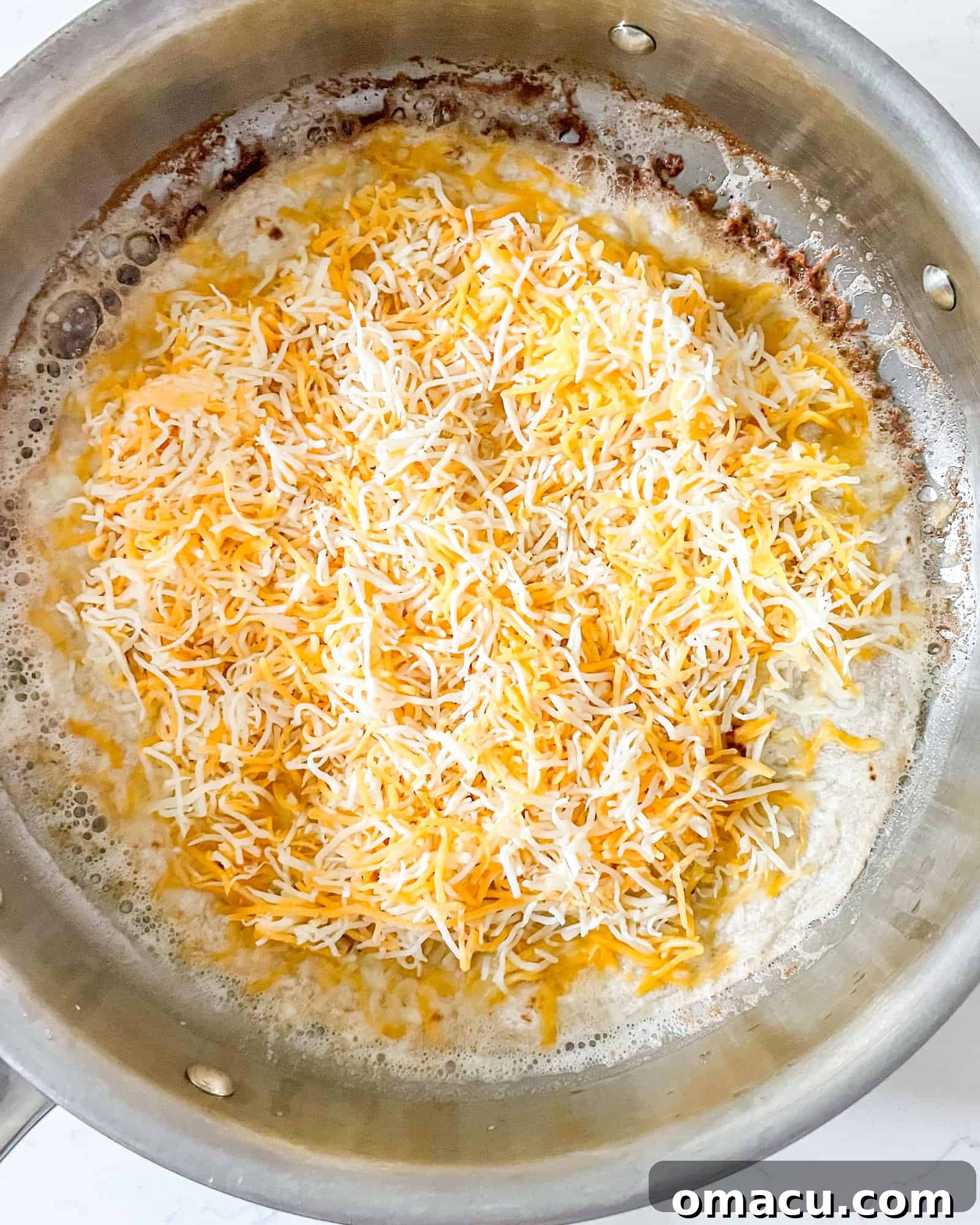 cheese on top of a flour tortilla in a frying pan.