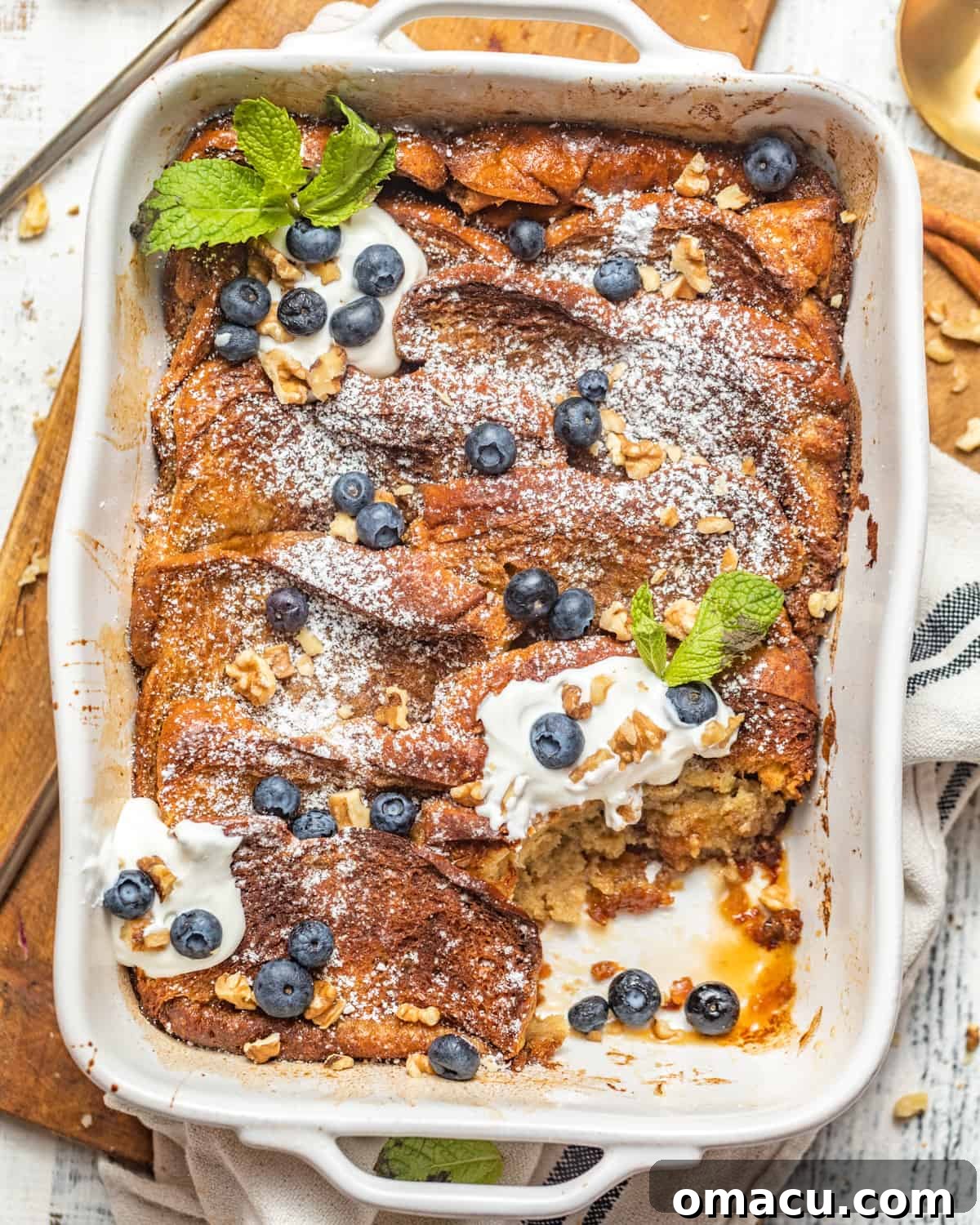 Brioche French toast casserole adorned with fresh blueberries and fluffy whipped cream, served in a rustic baking dish.