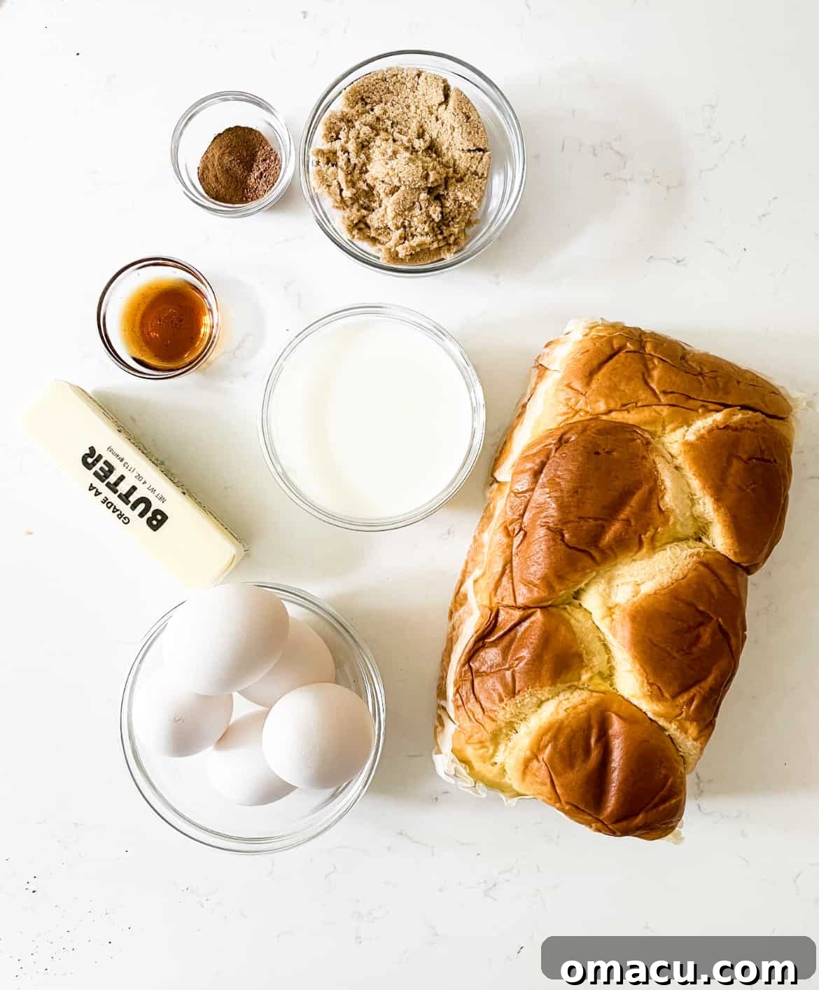 A vibrant flat lay of all the essential ingredients for French toast casserole: a loaf of brioche bread, brown sugar, butter, eggs, milk, cinnamon, nutmeg, and vanilla extract.