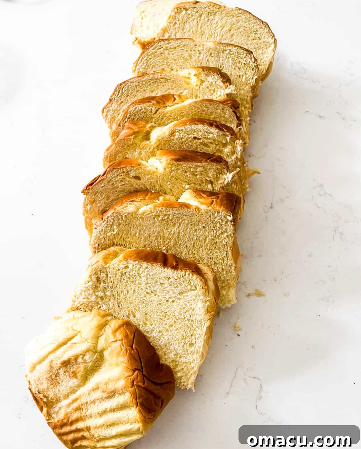 Thick slices of brioche bread arranged neatly on a white table, ready for the French toast casserole.