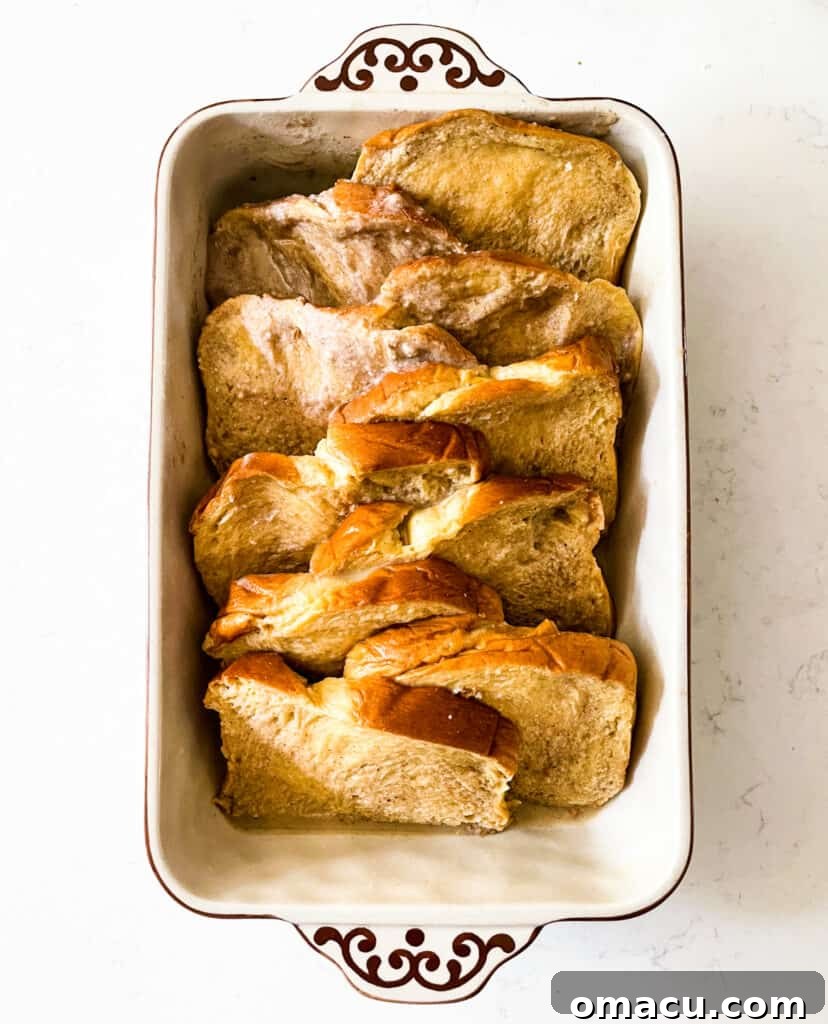 A casserole dish filled with prepped brioche bread slices soaking in custard, ready for baking.