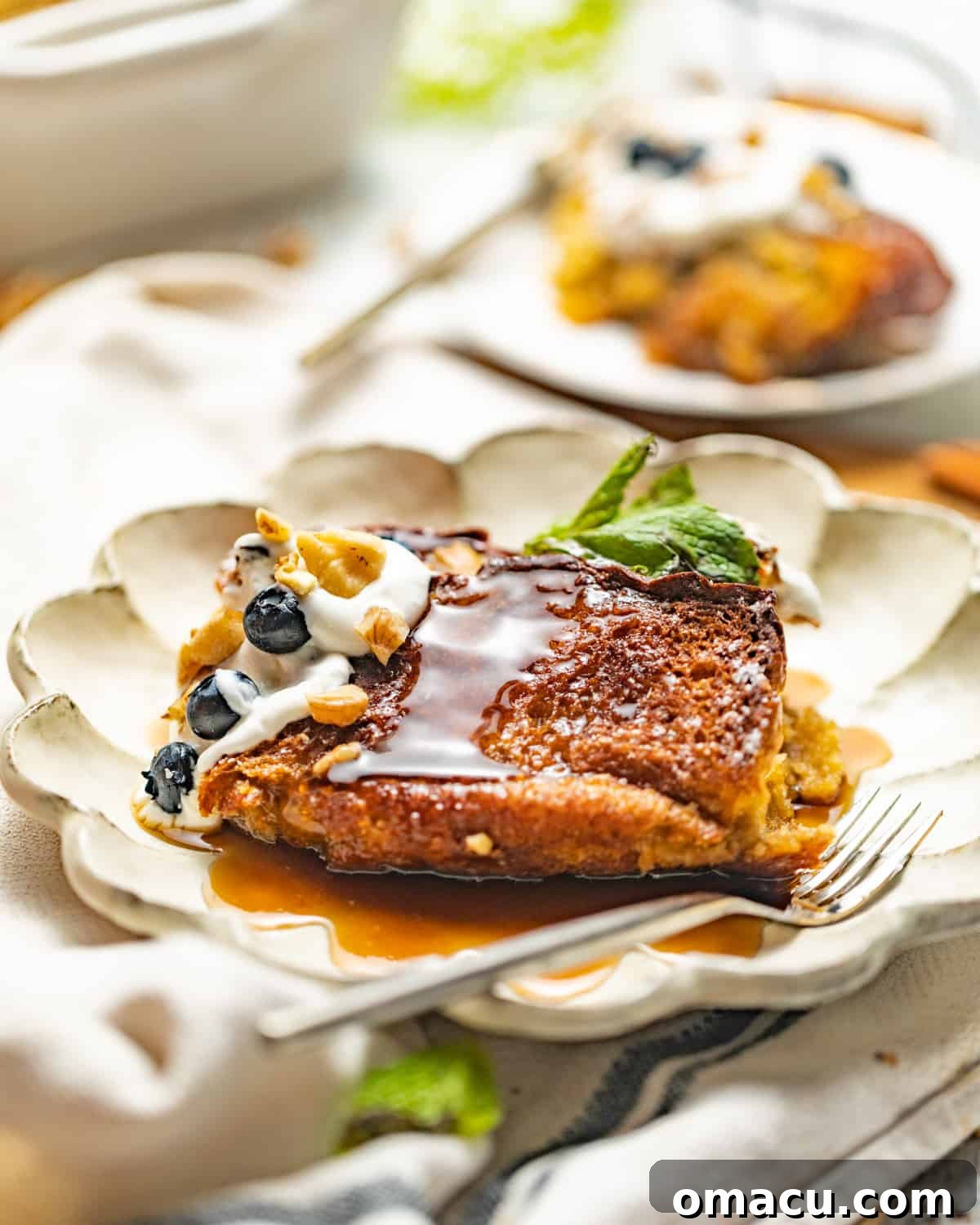 Individual slices of brioche French toast casserole elegantly plated, topped with whipped cream, fresh blueberries, and a generous drizzle of maple syrup.
