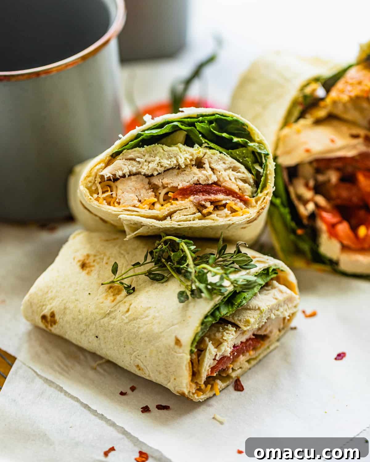 A chicken bacon ranch wrap, perfectly sliced in half, leaning against a rustic blue cup.