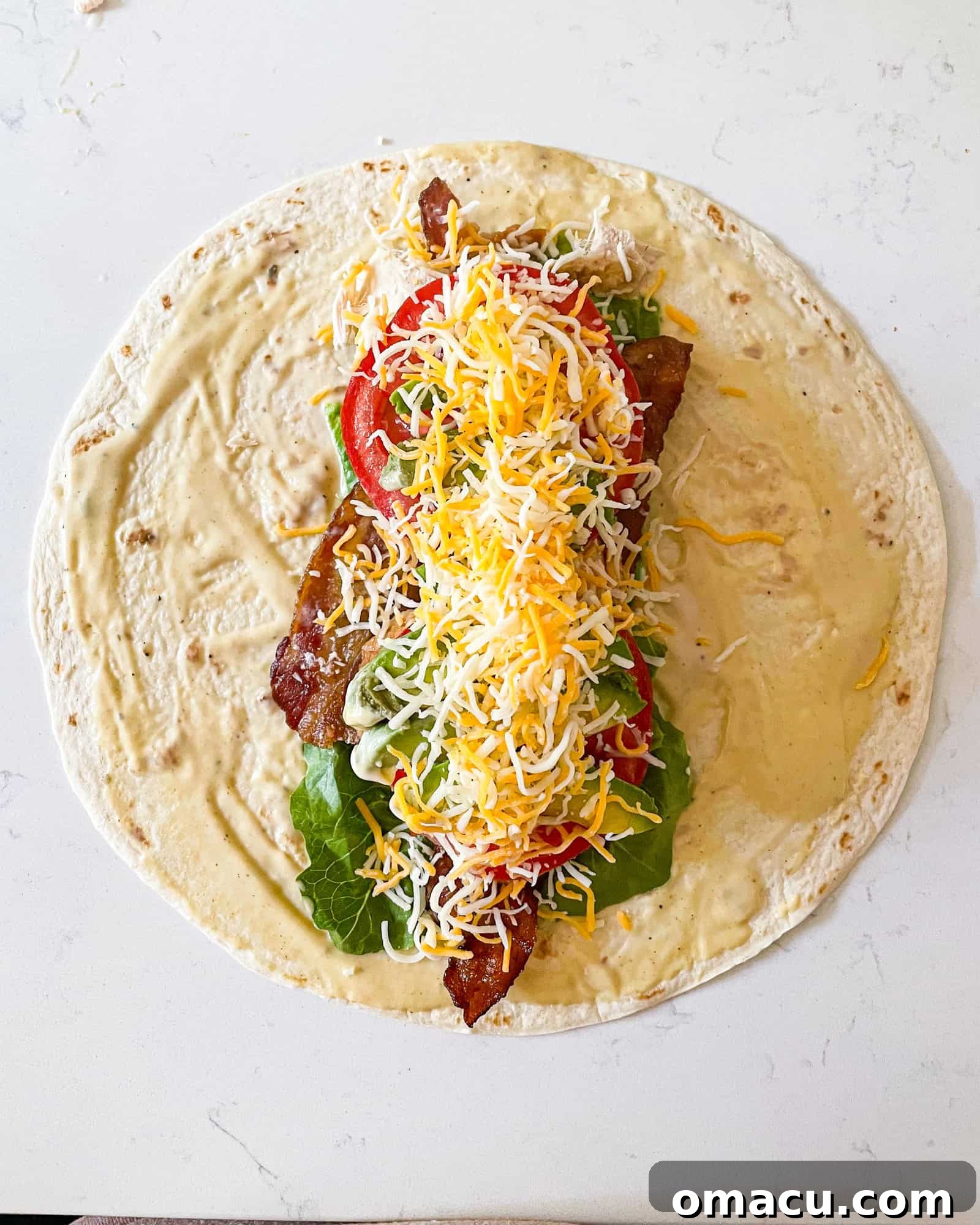 A tortilla filled with layers of fresh lettuce, crispy bacon, seasoned chicken, ripe tomatoes, creamy avocado, and shredded cheese.