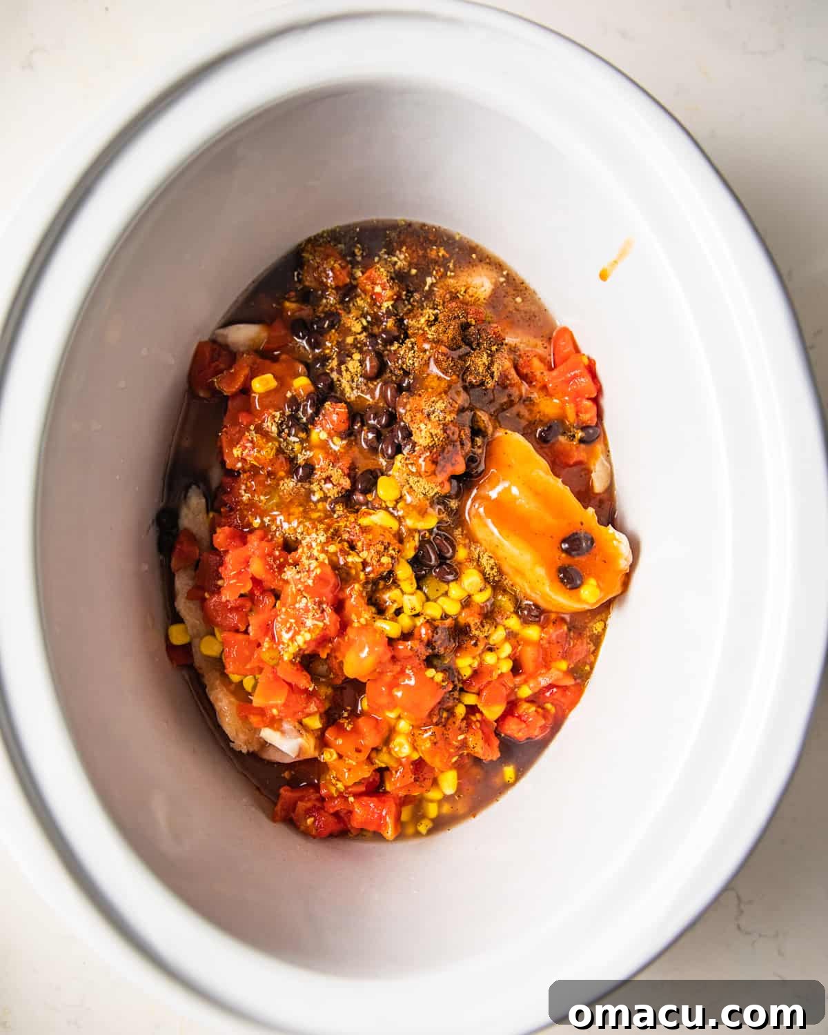 Raw chicken, tomatoes, enchilada sauce, black beans, sweet corn, and various seasonings beautifully arranged in a crockpot, ready for slow cooking.