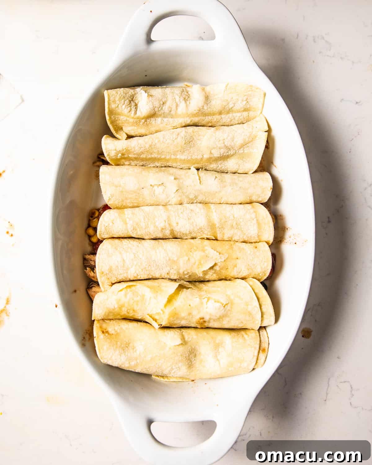 Partially assembled chicken enchiladas neatly arranged in a casserole dish, ready for the next step of preparation.