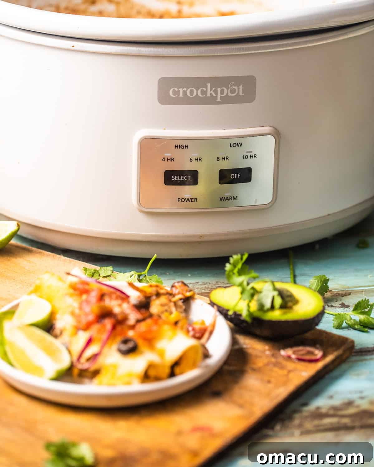 A slow cooker in the background, subtly out of focus, with a small plate of perfectly cooked chicken enchiladas in the foreground, garnished and ready to eat.