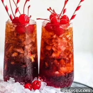 Two Roy Rogers drinks in a tall glass with paper straws and cherries.