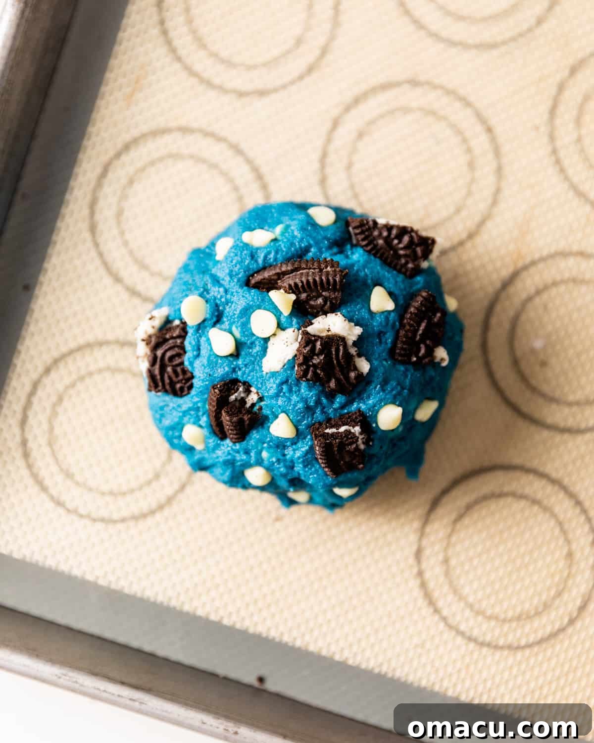 A cookie dough ball with crushed Oreo pieces on top, adding texture and visual appeal before baking.