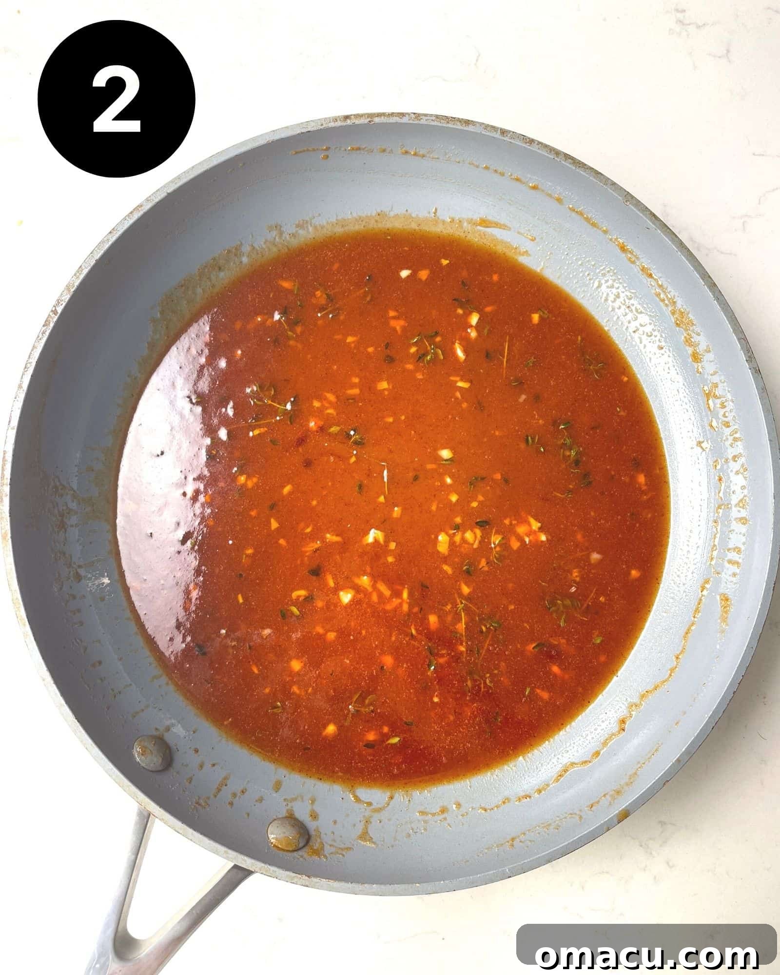 Honey sriracha sauce simmering gently in a small skillet on the stovetop.
