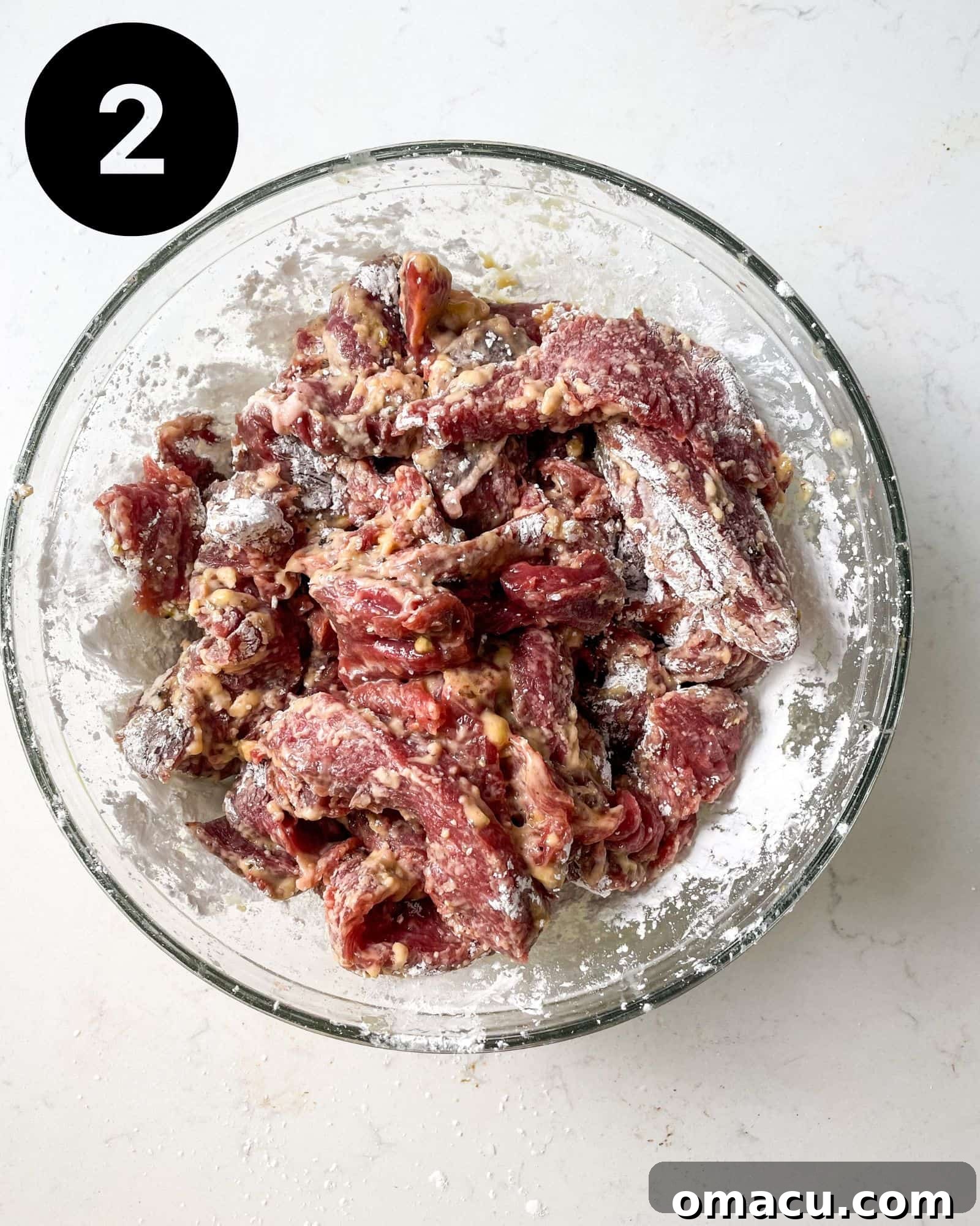 Sirloin steak strips generously tossed and coated in corn starch, egg, and a blend of seasonings in a mixing bowl.