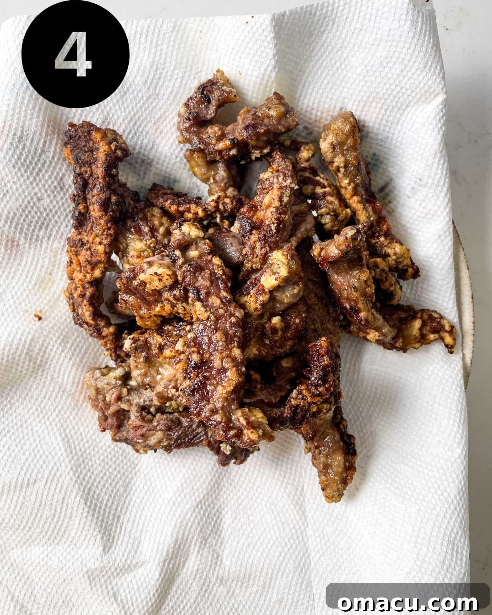 Freshly fried crispy chilli beef strips resting on a paper towel-lined plate to absorb excess oil.