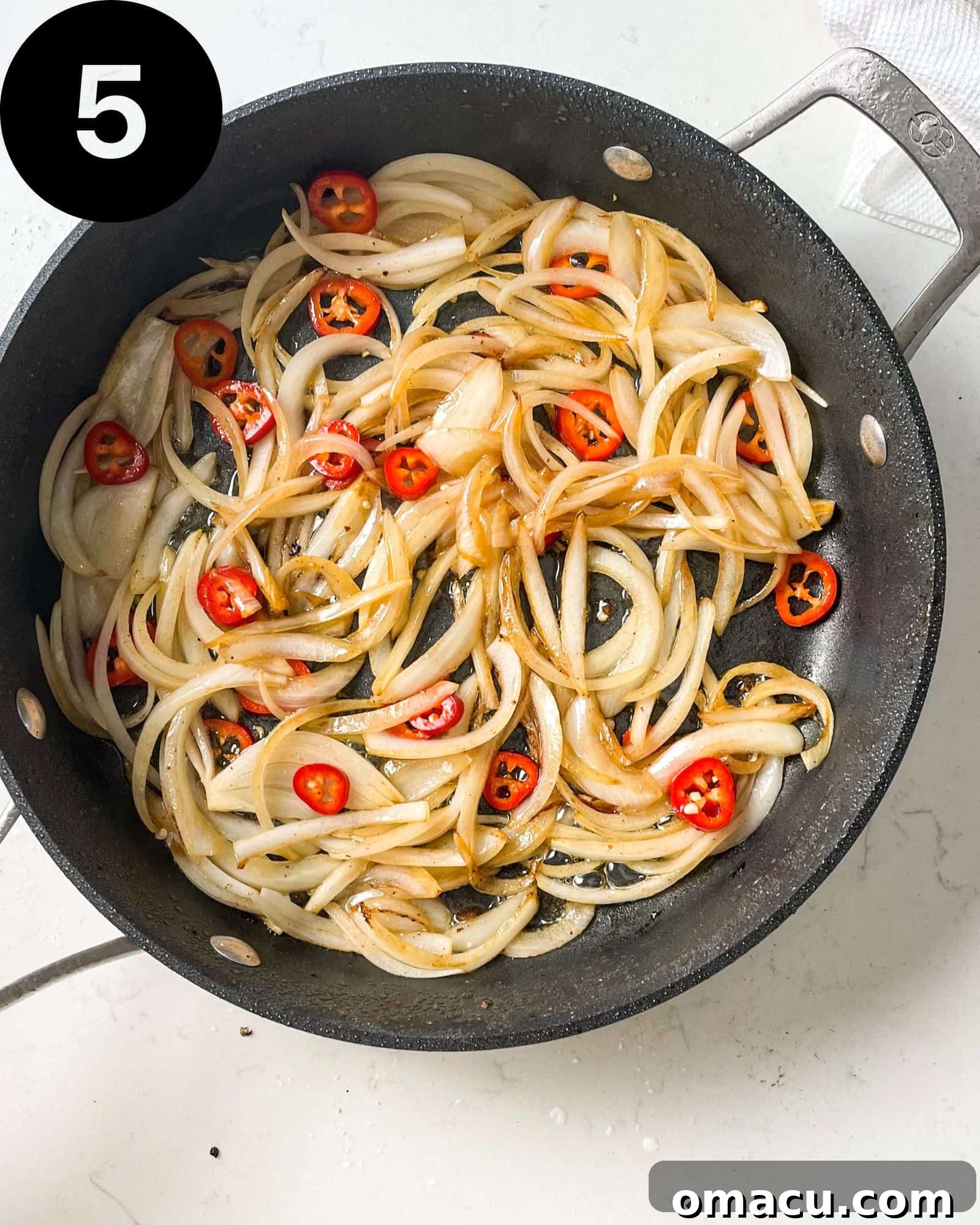 Sautéed onions, vibrant red chillies, aromatic grated ginger, and fragrant diced garlic cooking in a pan.
