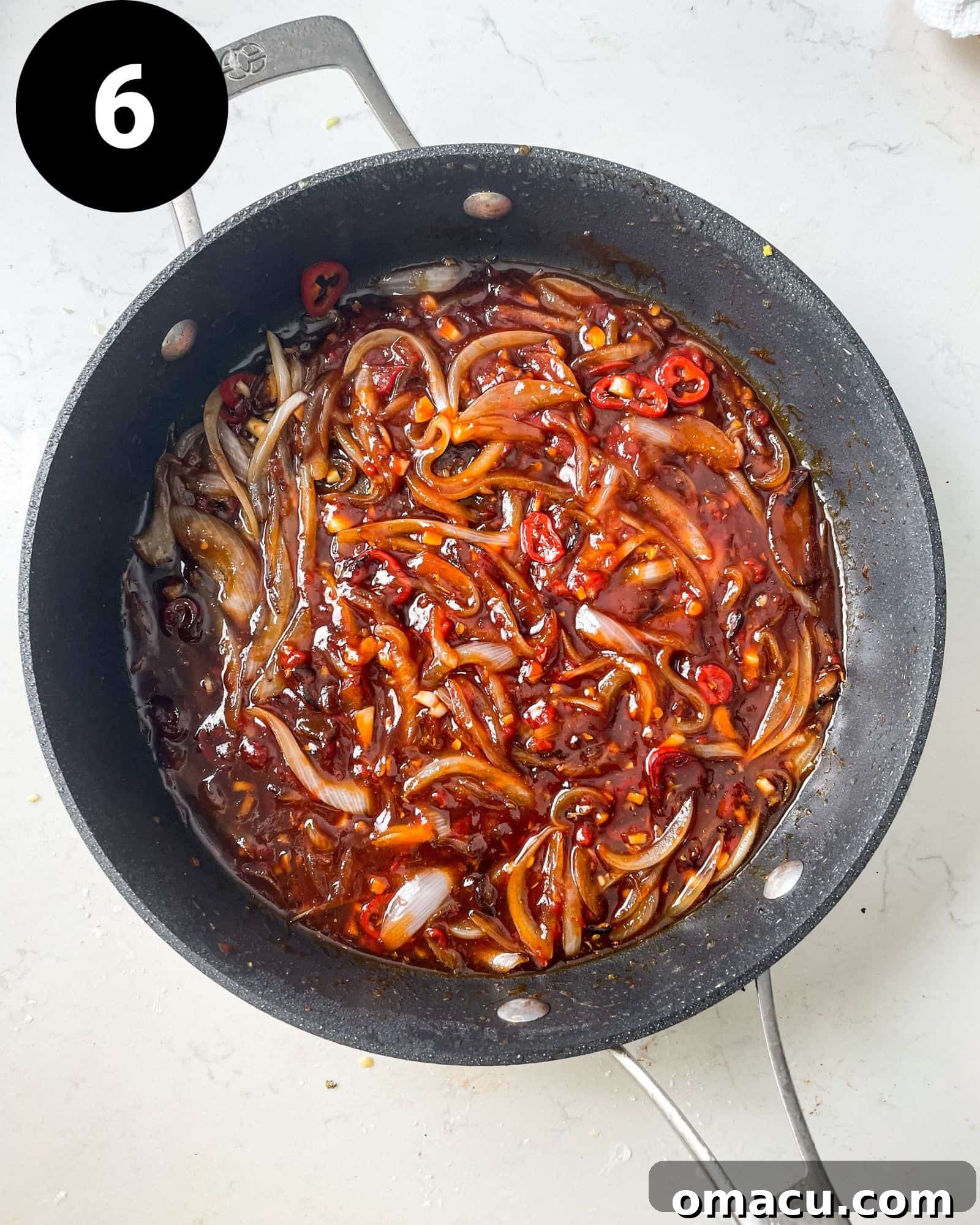 Sweet chilli sauce blending with sautéed onions and chillies in a hot pan, creating a vibrant sauce base.