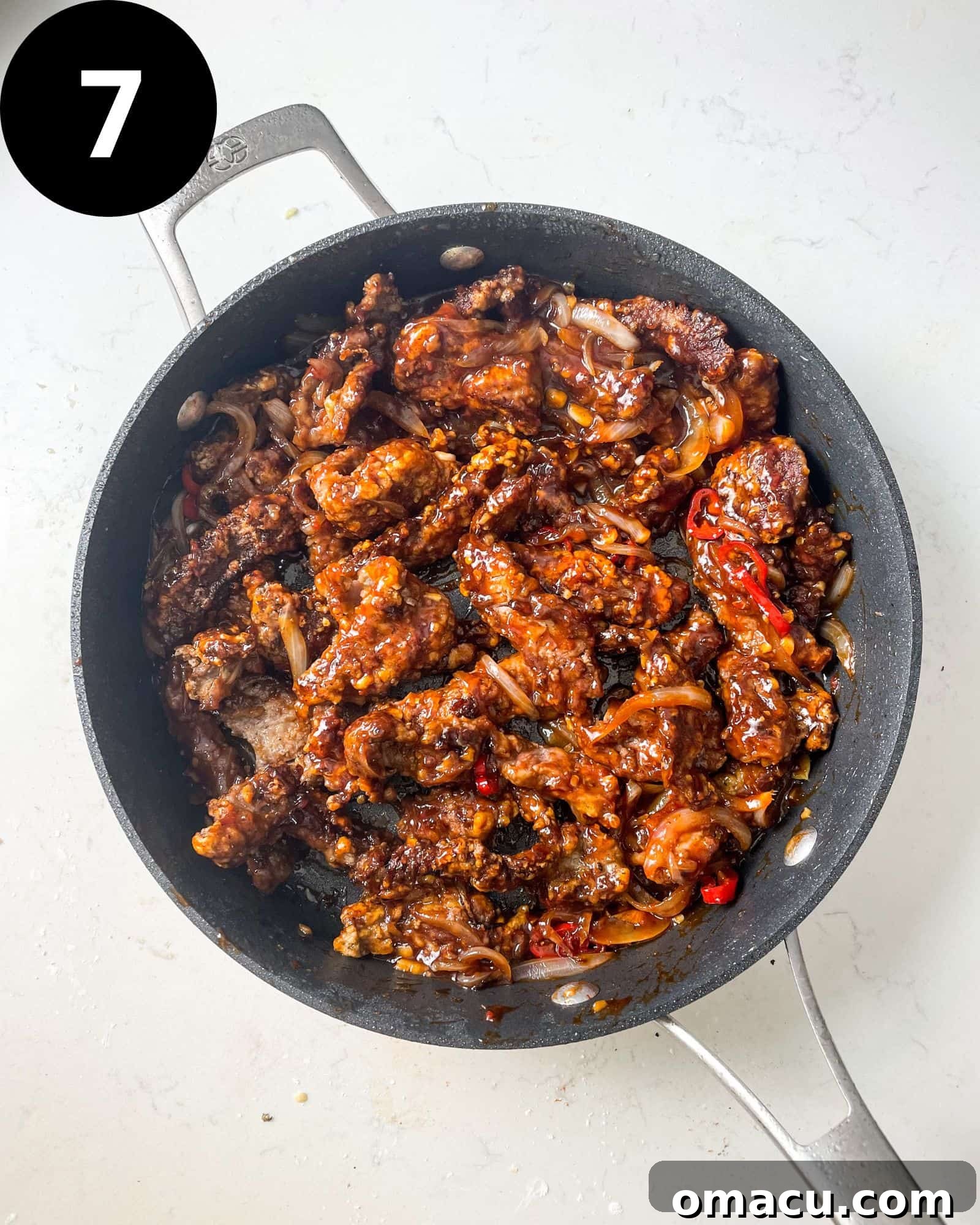 Crispy chilli beef strips glistening in a pan, thoroughly coated with a rich, sweet chilli sauce.