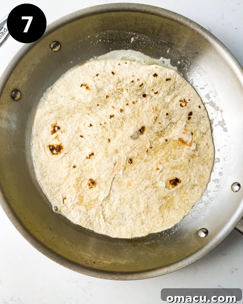 a tortilla dipped in birria consomme in a pan, ready for filling.