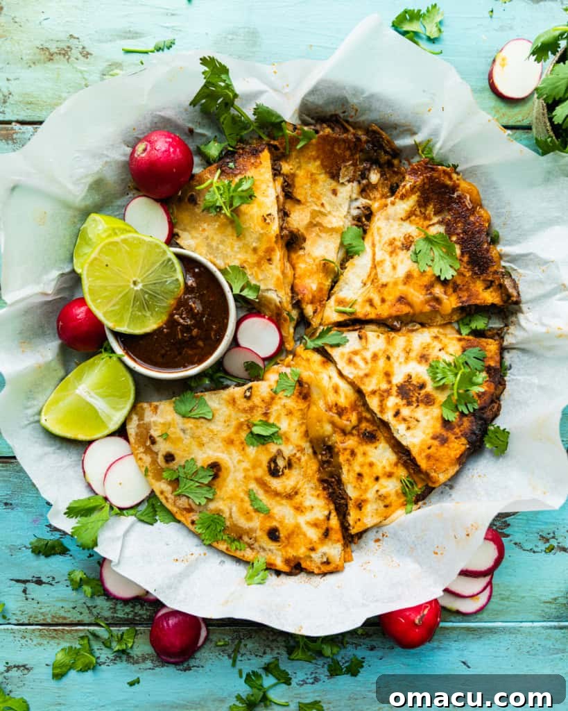 birria quesadilla on a piece of parchment paper with a bowl of birria consume, highlighting its presentation.