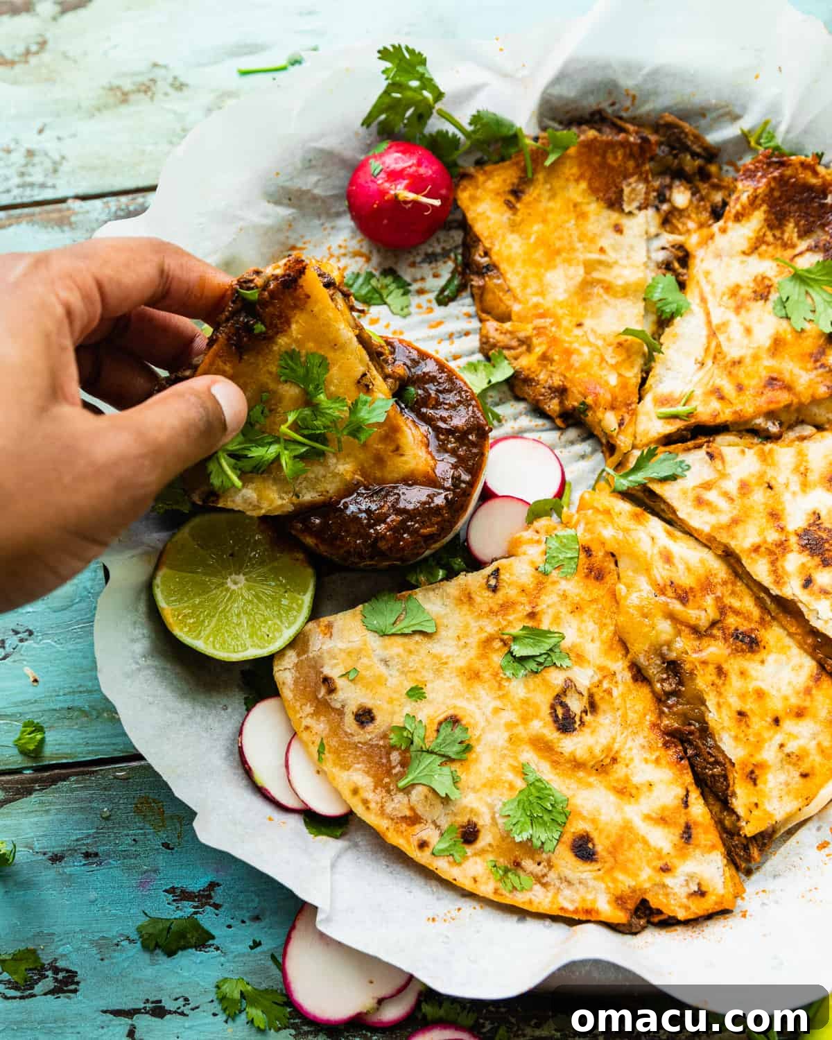 a hand dipping a slice of the birria quesadillas into the birria consume, showing the rich broth.